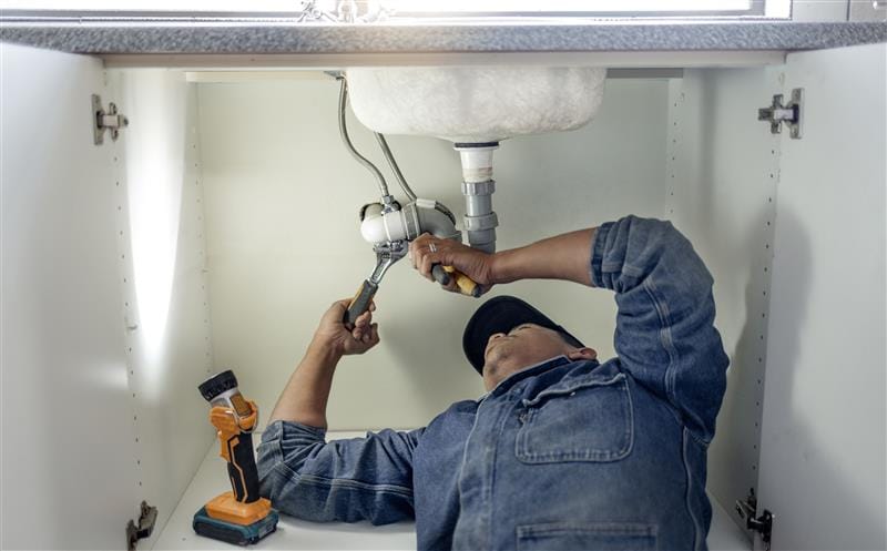 Plumber repairing pipes beneath a bathroom sink in Bellflower